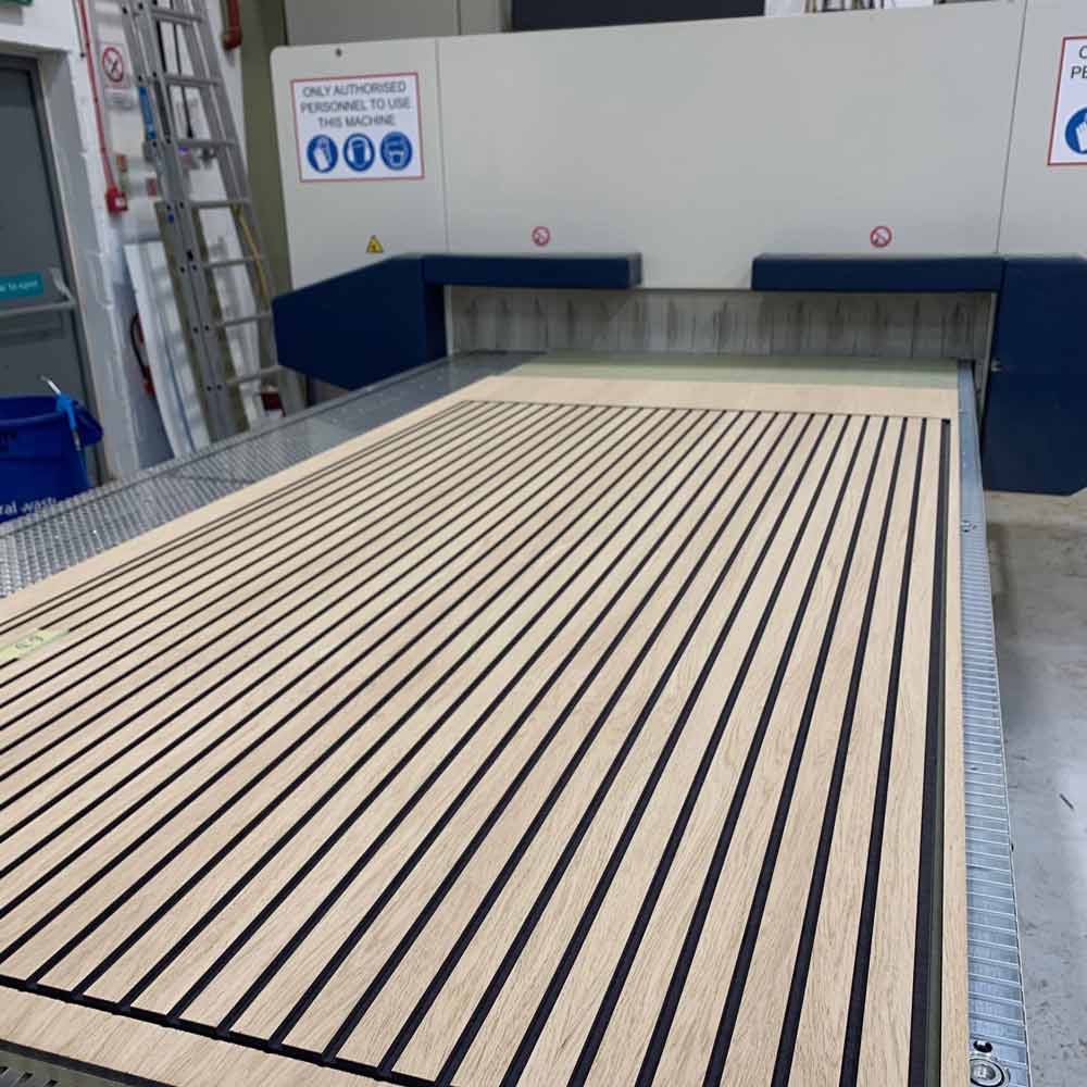 a full sheet of oak veneered black dyed mdf slat wall laying on the bed of a cnc machine