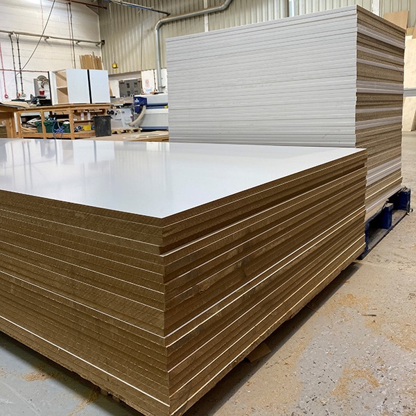Two stacks of White Melamine Faced board the one in the foreground are uncut MF MDF the one behind is Melamine Faced Chipboard which has been cut to size and edged with ABS Edging