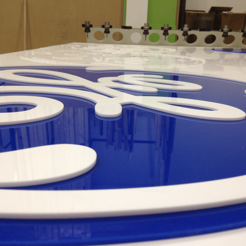 A GE logo cut from white and blue perspex and laying on top of a CNC machine