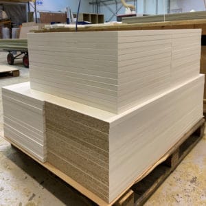 A stack of white Melamine faced chipboard panels cut to size and edged sat in a workshop environment