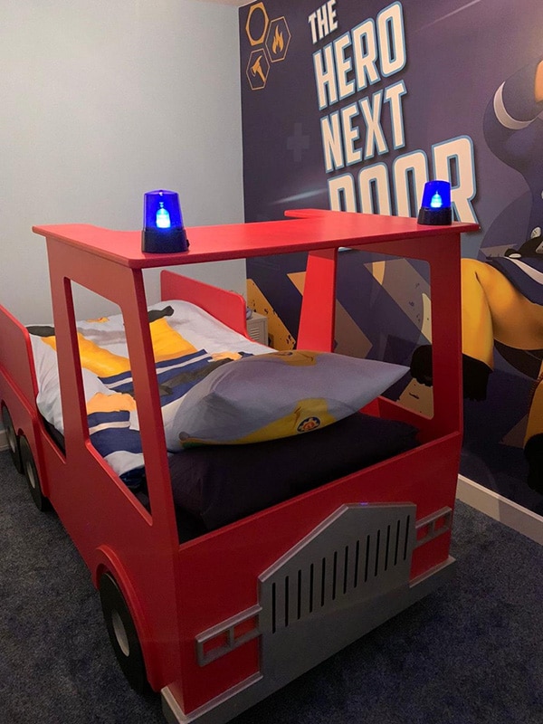 A child's Fire engine shaped bed made from MDF featuring blue flashing lights on the roof