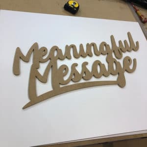 CNC cut MDF letters spelling meaningful message sitting on a white board on workshop bench