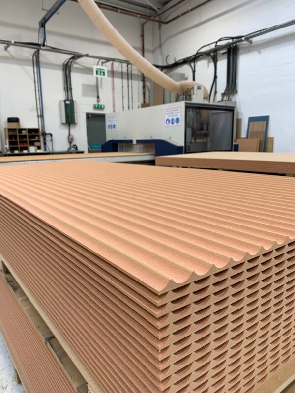 A large stack of Standard Fluted Fire Rated MDF Panels in front of a CNC Machine