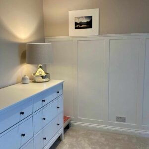 Light grey wall panelling with a white chest of drawers in front