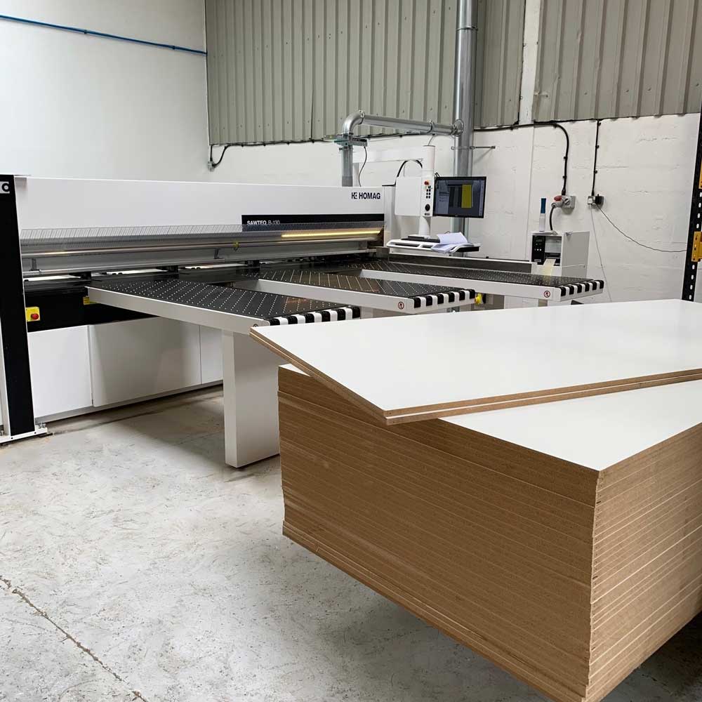 a stack of white melamine board in front of a homag beam saw