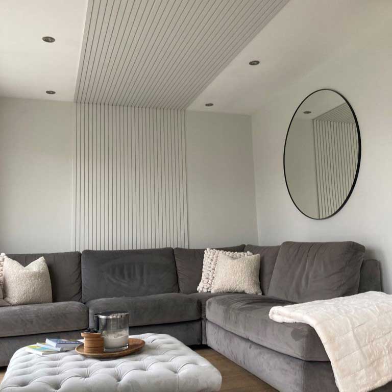 grey painted mdf slat wall panelling strips in the centre of wall and across the ceiling, in front of a grey L shape sofa