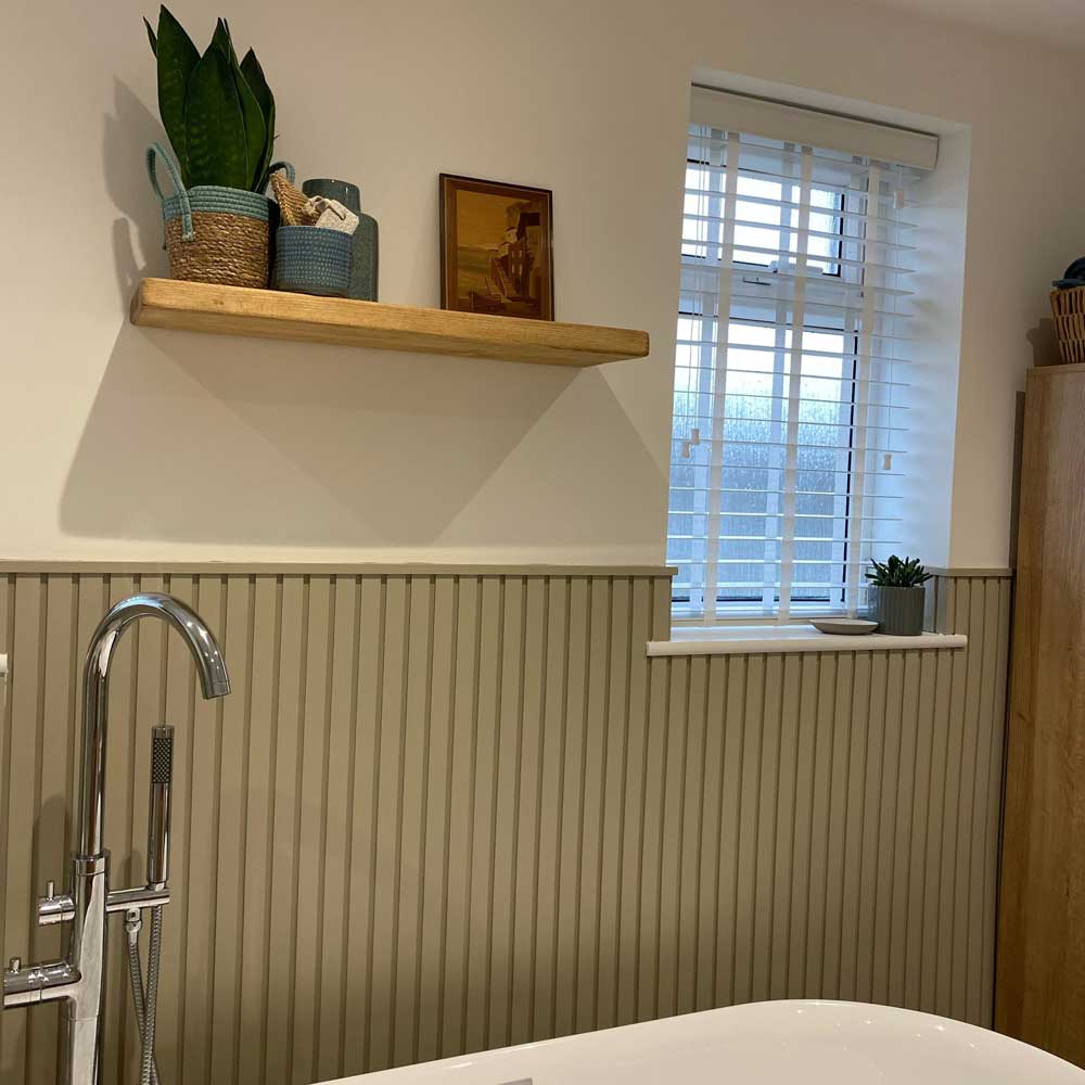 green painted mdf slatted panels in a bathroom situated behind a bath tub, below a shelving unit and window